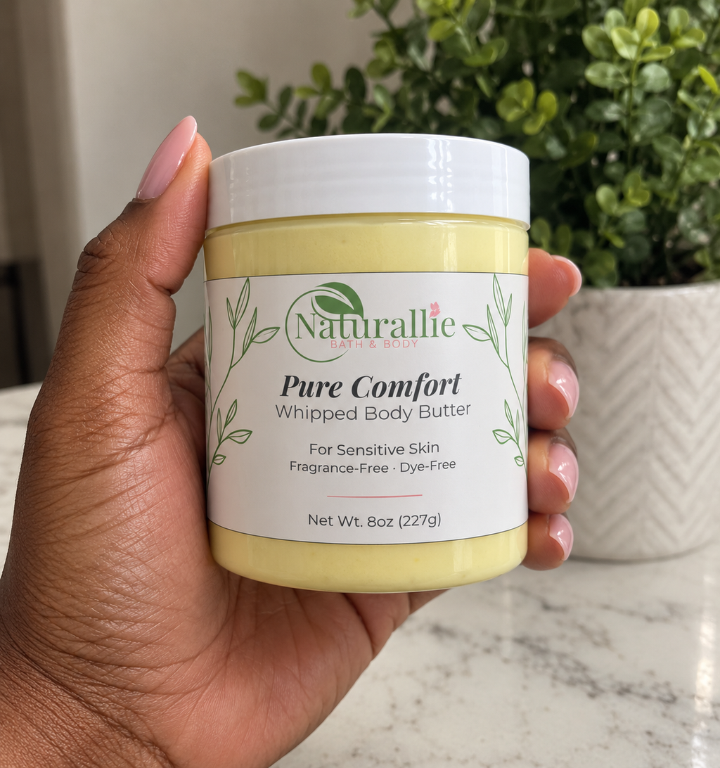 A hand holding a jar of Naturallie Pure Comfort Whipped Body Butter, with a potted green plant in the background.